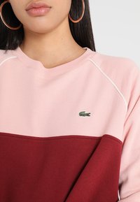 Rosa und burgunderfarben farblich abgesetzter Sweatshirt mit Rundhalsausschnitt, ausgestattet mit einem kleinen grünen gestickten Krokodil-Logo und weißen Akzentnähten.