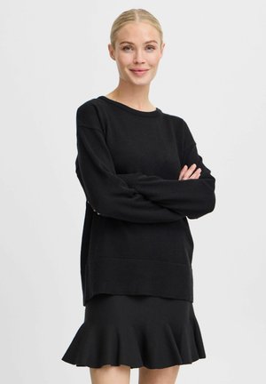 Schwarzer Strickpullover mit langen Ärmeln, rundem Halsausschnitt und geripptem Saum; kombiniert mit einem schwarzen, schwingenden Rock. Glatte Textur, schlichtes Design.