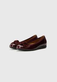 Des ballerines bordeaux en cuir verni brillant, avec un détail en daim texturé en forme de nœud au niveau des orteils et une semelle en caoutchouc noir.