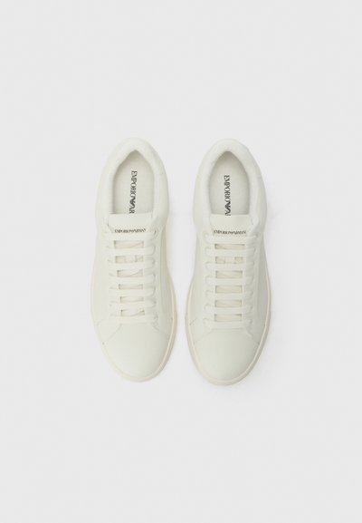 White leather sneakers with rounded toes, flat laces, and a soft lining. Features subtle branding inside the tongue. Smooth texture.