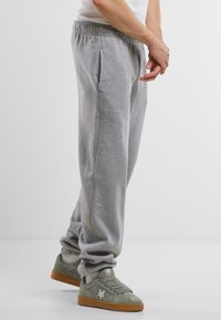 Pantalons de survêtement gris avec une taille élastique, des poignets fuselés, des poches latérales, associés à des chaussures de sport vertes avec des accents de logo blancs.
