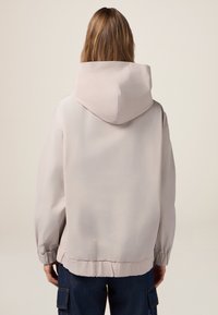Lichtgrijze hoodie-jack met een ontspannen pasvorm, elastische manchetten en een elastische taille. Zachte textuur met minimale naden en een eenvoudig, strak ontwerp.