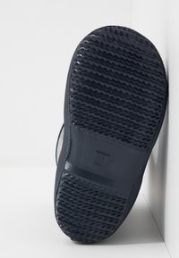 Semelle de chaussure en caoutchouc noir avec un motif de relief texturé et une indentation rectangulaire marquée "25." Positionnée sur un fond clair.