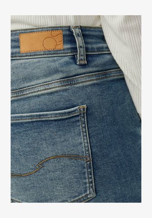 Verbleekte blauwe spijkerbroek met een leren cognackleurig stukje op de tailleband, met een enkele achterzak met gebogen stiksel.