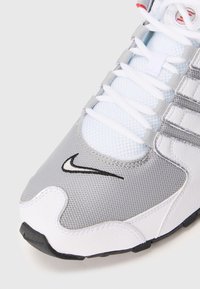 Nike kedas ar pelēko acu materiālu un baltu sintētisku materiālu, melnā apdare, taisnas šņores un teksturēta gumijas zole.