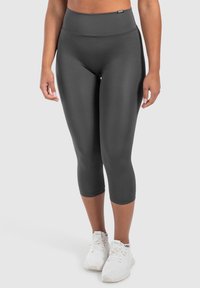 Leggings capri grigi, aderenti, con vita alta e materiale liscio, abbinati a scarpe da ginnastica bianche.