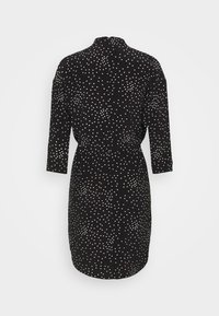 Robe noire longueur genou à pois blancs, manches longues et taille légèrement froncée, vue de dos.