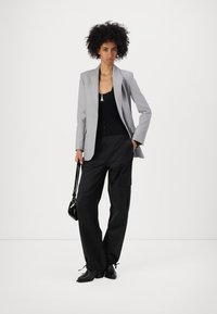Grå rutete blazer over en svart topp, kombinert med løse svarte cargo-bukser. Modellen holder en liten svart veske og har på seg svarte høye støvler.