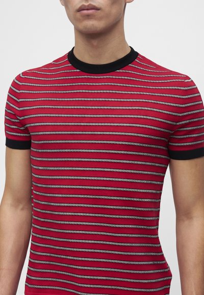 Homme portant un t-shirt rouge ajusté avec des rayures horizontales noires et blanches et une bordure noire au col et aux manches.