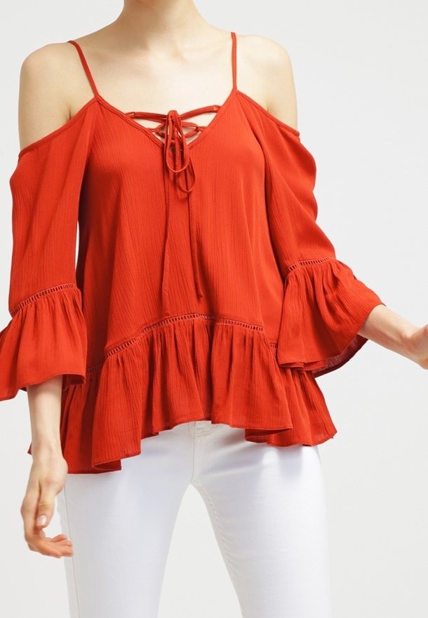Blouse rouge à épaules dénudées avec des manches évasées, devant à lacets et ourlet froncé. Fabriquée en tissu texturé, offrant une coupe ample.