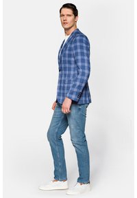 Niebieska marynarka w kratę z klapkami, pojedynczym guzikiem i dwiema przednimi kieszeniami, zestawiona z jasnymi dżinsami i białymi trampkami.