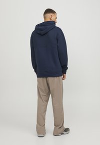 Marineblauer Kapuzenpullover mit strukturiertem Einsatz, Kängurutasche, verstellbarer Kapuze; kombiniert mit beigen, lockeren Hosen und grauen Sneakers.