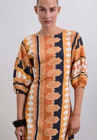 Robe à motifs multicolores présentant des teintes orange, noire et blanche, avec une coupe ample, des manches bouffantes et un col rond.