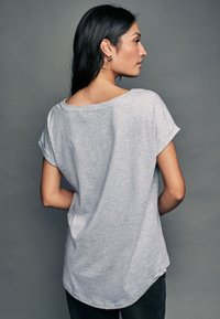 T-shirt gris à manches courtes avec un col rond, une coupe décontractée et des manches retroussées, fabriqué dans un tissu doux. L'ourlet est légèrement plus long à l'arrière.