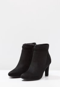 Botas de tobillo de ante negro con punta afilada, tacón de 9 cm, cremallera lateral y acentos texturizados decorativos a lo largo del cuello.