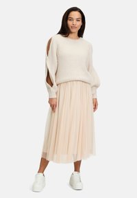 Maglione lavorato a maglia beige chiaro con dettagli sulle spalle scoperte, abbinato a una gonna plissettata rosa chiaro e sneaker bianche con platform.