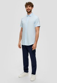 Lichtblauw kortemmershirt met een knoopsluiting aan de voorkant, gecombineerd met marineblauwe broek en witte sneakers. De stof lijkt glad met een subtiele glans.