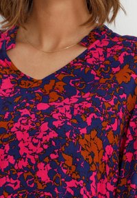 V-ringad topp med ett blommönster i rosa, marinblå och bruna nyanser, gjord av ett glattyg med en mjuk textur.