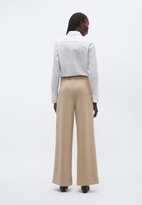 Valge triibuline pluus struktureeritud kraega, kombineeritud beežide laia säärega pükstega. Komplekti iseloomustavad sile tekstuur ja puhtad jooned.