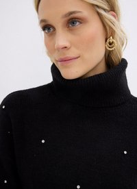 Maglione a collo alto nero con un tessuto lavorato e dettagli decorativi in strass sparsi. Indossato con grandi orecchini a cerchio d'oro.