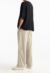 Top nero a maniche corte con effetto rigato abbinato a pantaloni beige larghi. L'outfit presenta una silhouette rilassata e un design minimalista.