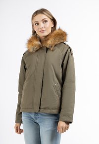 Oliven grøn frakke med hætte i pels, lynlåslukning foran, to sidelommer og en afslappet pasform. Stoffet virker glat og let.