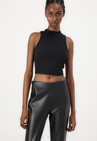 Black ribbed sleeveless crop top with a high neck, paired with smooth black faux leather high-waisted pants, emphasizing a fitted silhouette.