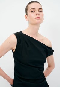 Schwarzes einseitiges Kleid aus glattem Stoff, mit einem drapierten Design und subtiler Textur, das den Schulter- und Schlüsselbeinbereich betont.