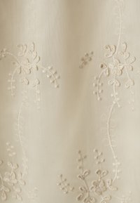 Embroidered fabric featuring intricate, delicate floral designs in a soft cream color, with a smooth texture and subtle sheen.