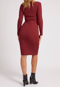 Abito midi in raso bordeaux a coste con maniche lunghe, silhouette aderente e scollatura rotonda. Indossato con stivaletti neri alla caviglia con dettaglio di zip.