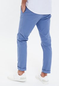 Chinos azzurri chiari con una vestibilità slim, dotati di tasche laterali, risvolti e abbinati a sneakers bianche. Texture liscia, design casual.