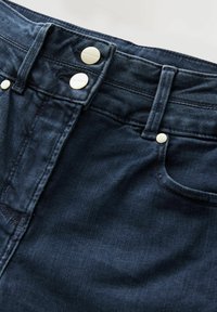 Jeans in denim blu scuro con taglio dritto, due bottoni metallici in vita e dettagli di cucitura discreti sulle tasche anteriori.