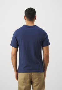 Marineblå bomulds T-shirt med rund halsudskæring og korte ærmer, set fra ryggen. Simpelt design, blød tekstur, ingen synlige mønstre eller accenter.