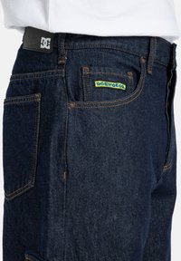Tmavomodré denimové nohavice s bežným strihom, s kontrastným prešívaním, koženou nášivkou na páse a multikolórovou štítkom na zadnej vrecku.