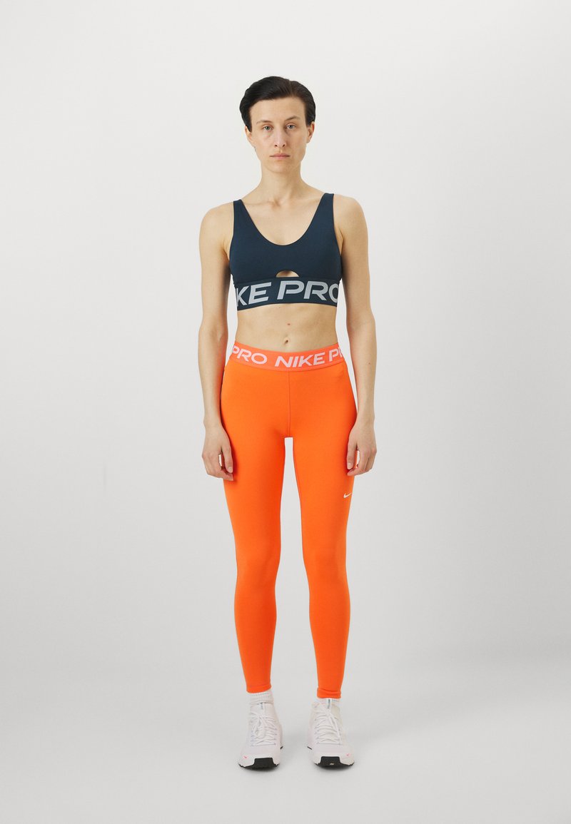 Nike Pro Sport-BH in Marineblau mit Ausschnitt, kombiniert mit leuchtend orangen Leggings mit Nike-Logo. Das Material ist dehnbar; das Design ist enganliegend.