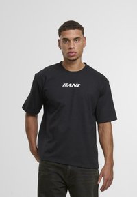 Black cotton t-shirt with a crew neck and short sleeves. "KANU" logo in white across the chest. Simple design, regular fit.