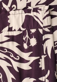 Close-up of purple and white fabric with floral and leaf patterns showing a waistband and stitched seam.