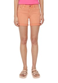 Brzoskwiniowe dżinsowe szorty z podwiniętymi nogawkami, kieszeniami z przodu i zapięciem na guzik. Nosenie ich z jasnoróżowymi sandałami z szerokimi paskami.