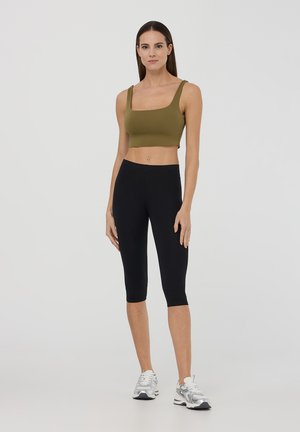 Top corto color verde oliva con spalline larghe, abbinato a leggings neri a lunghezza ginocchio. Design minimalista con una texture liscia e elastica.