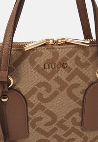 Borsa marrone con motivo a fantasia, dettagli in pelle, accessori in tono oro e chiusura con zip. Presenta dettaglio con logo e manici corti.