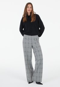 Knitted black cowl-neck sweater paired with gray checked wide-leg trousers featuring black and white lines and pointed black heels.