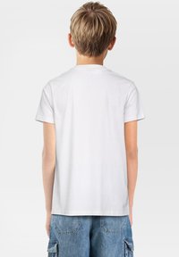 Camiseta de algodón blanca de manga corta y cuello redondo, vista desde la parte de atrás, combinada con pantalones cortos de denim, con una textura simple y suave.