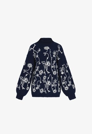 Merinovillaneulko, jossa on monimutkainen valkoinen kukkakirjonta, korkea kaulus ja volyymiset hihat. Pehmeä materiaali, jossa on selkeät kuviot.