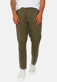 Joggers in lino verde oliva con cintura elastica e cordoncino. Design con gamba affusolata e spacco laterale, abbinati a sneaker bianche.