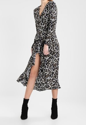 Vestido negro de manga larga con estampado floral blanco, escote en V profundo, dobladillo con volantes y abertura lateral, combinado con botines negros.