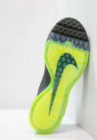 Suola di scarpa sportiva nera con motivo a nido d'ape, accenti giallo-verdi traslucidi e un logo scuro ben visibile. Costruzione in gomma testurizzata.