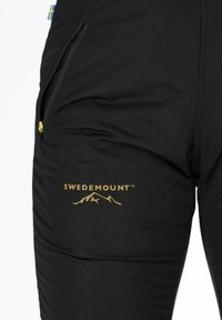 Black thermal pants featuring a zippered pocket, gold "SWEDEMOUNT" logo, and a mountain design, offered in a stretchy, smooth fabric.