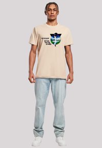 Beige cotton t-shirt featuring a graphic print of a figure with the text "David Bowie The Man Who Fell to Earth" in black.