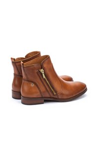 Botas de cuero marrón hasta el tobillo con cremallera lateral, textura suave, punta redondeada, tacón apilado y un pequeño logotipo en el lateral.