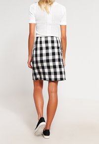Černobílá kostkovaná sukně, ke kolenům, vyrobená z tkaniny. V kombinaci s bílým tričkem krátkým rukávem a černými teniskami.